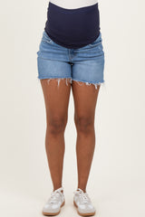 woman wearing a navy blue maternity top and distressed denim maternity shorts, showcasing a visible baby bump