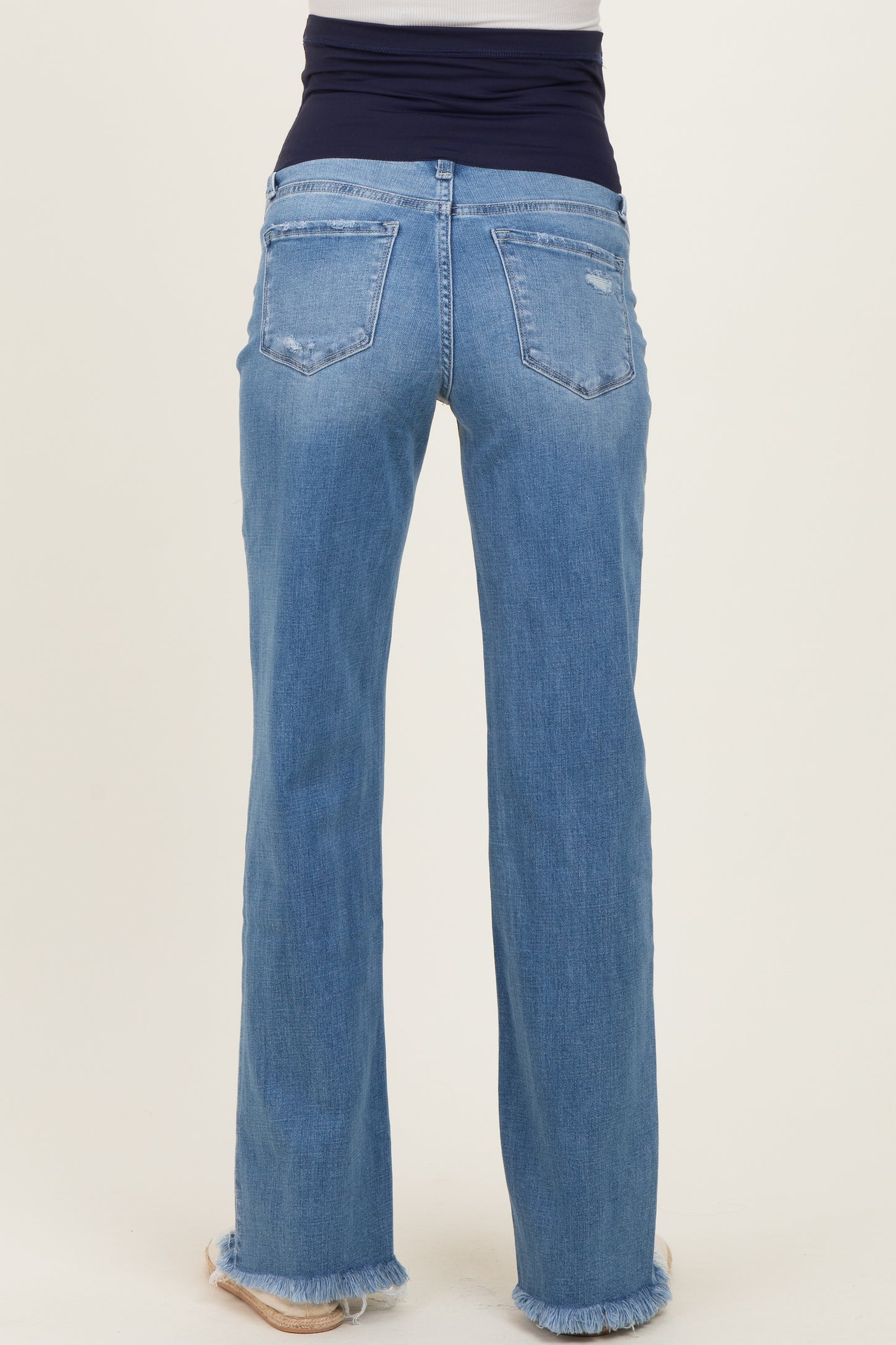 woman wearing light blue maternity jeans with a high waistband and frayed hem, facing away from the camera