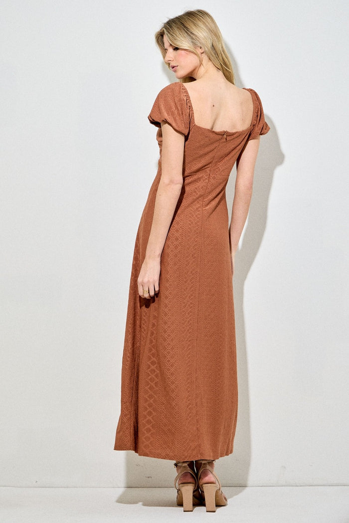 woman wearing a rust-colored maxi dress with puff sleeves and a back zip closure
