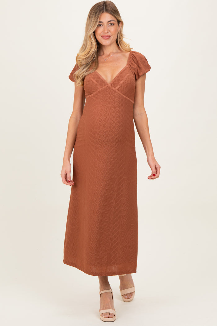woman wearing a rust-colored maternity maxi dress with puff sleeves and a plunging neckline, showing her baby bump