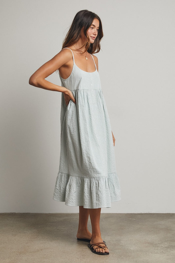 woman wearing a light green gingham print midi dress with a ruffled hem and spaghetti straps