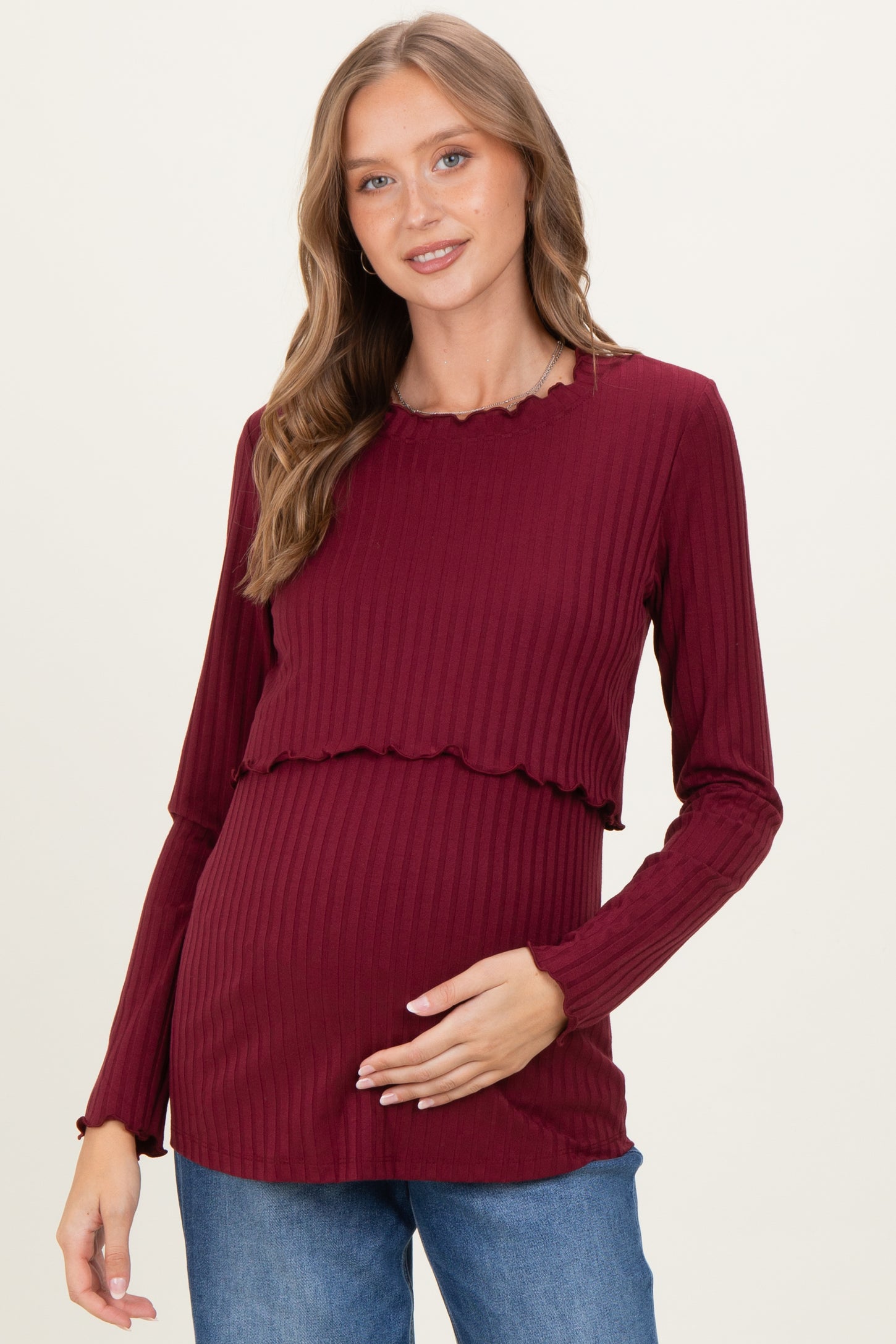 woman wearing a burgundy maternity top with ribbed texture and ruffled hem, holding her baby bump
