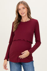 woman wearing a burgundy maternity top with ribbed texture and ruffled hem, holding her baby bump