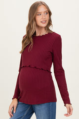 woman wearing a burgundy ribbed maternity top with ruffle details and a visible baby bump