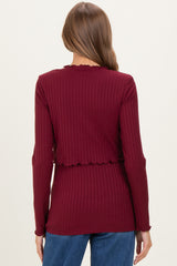 woman wearing a burgundy long sleeve maternity top with a ribbed texture and scalloped edges, shown from the back