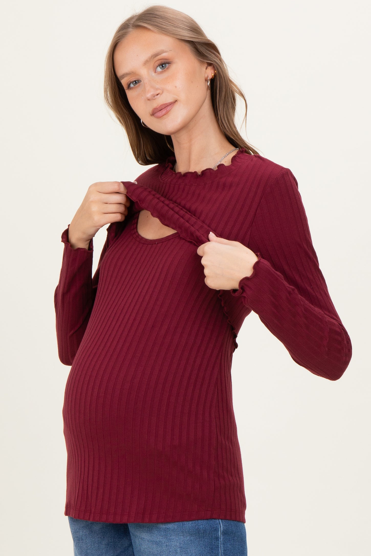 woman wearing a burgundy ribbed maternity top with ruffled neckline, showing a baby bump while lifting the fabric