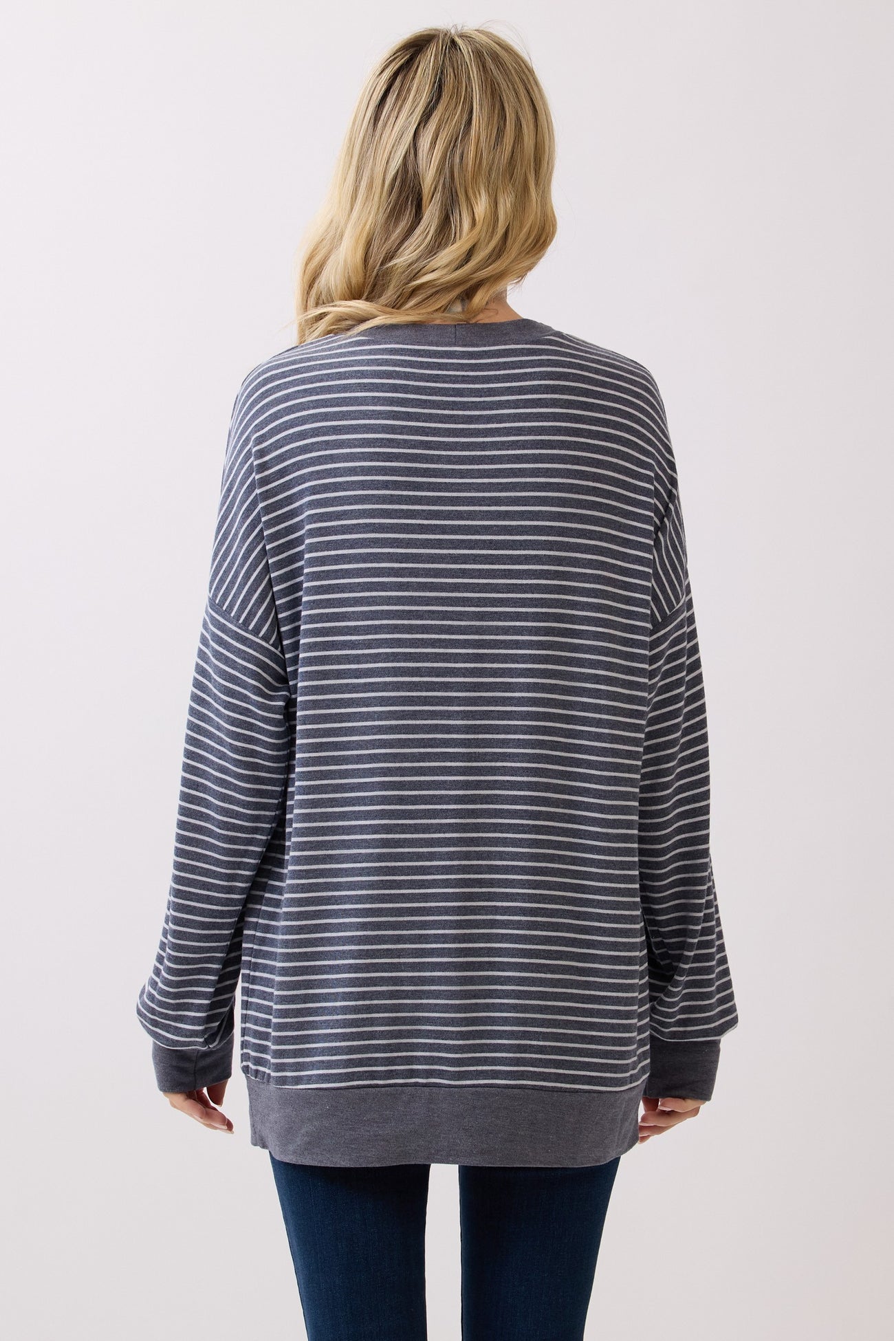 woman wearing a gray and white striped oversized sweater with long sleeves and a relaxed fit, seen from the back