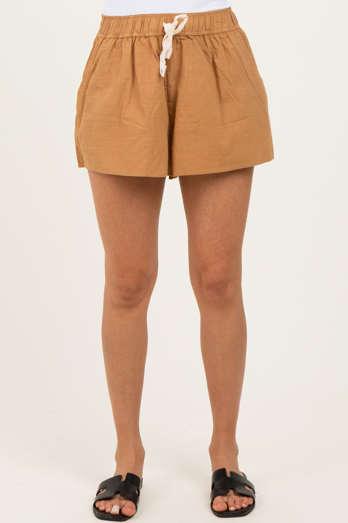 woman wearing light brown drawstring shorts with pockets and black slide sandals