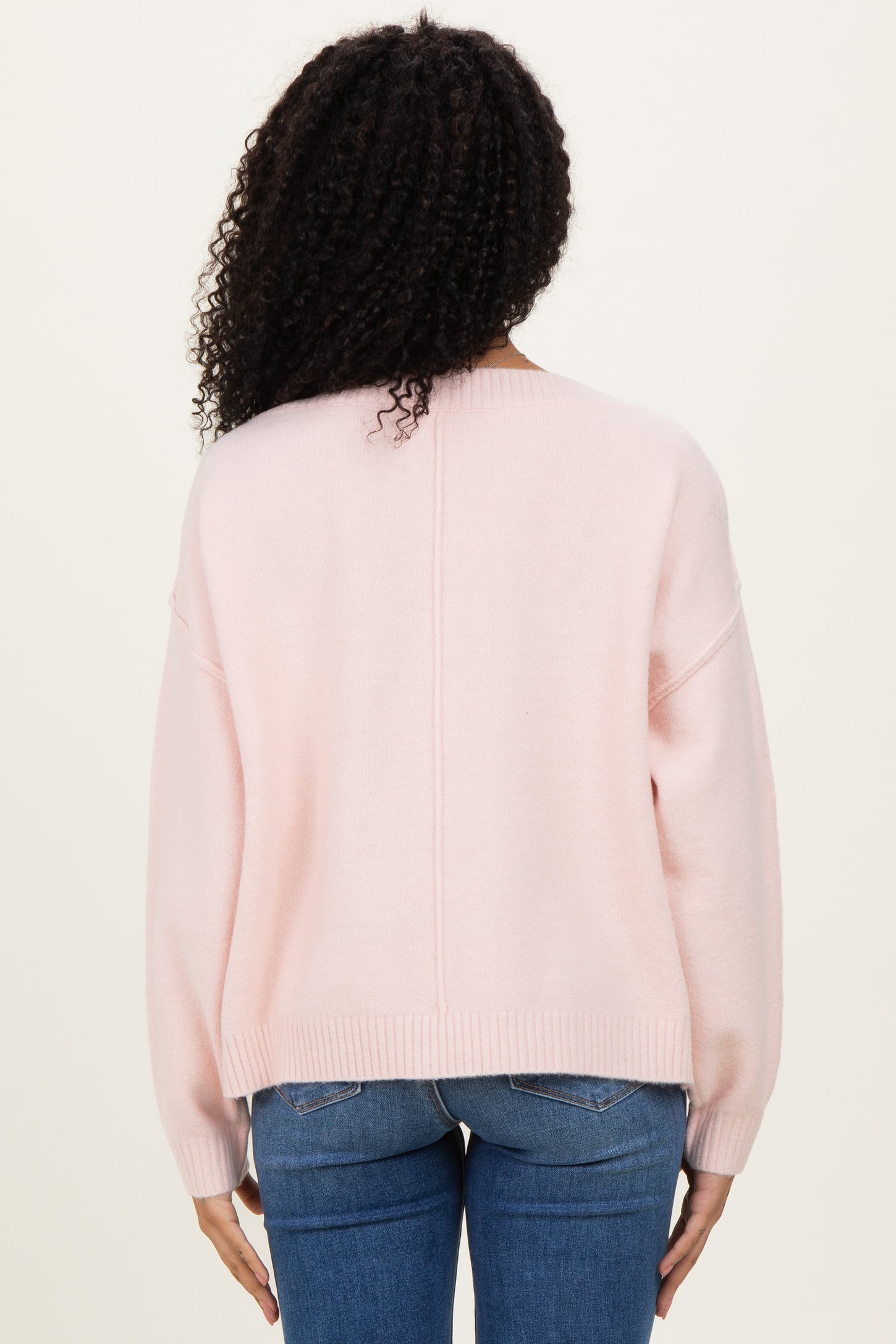 woman wearing a light pink oversized sweater with a relaxed fit and dropped shoulders, seen from the back