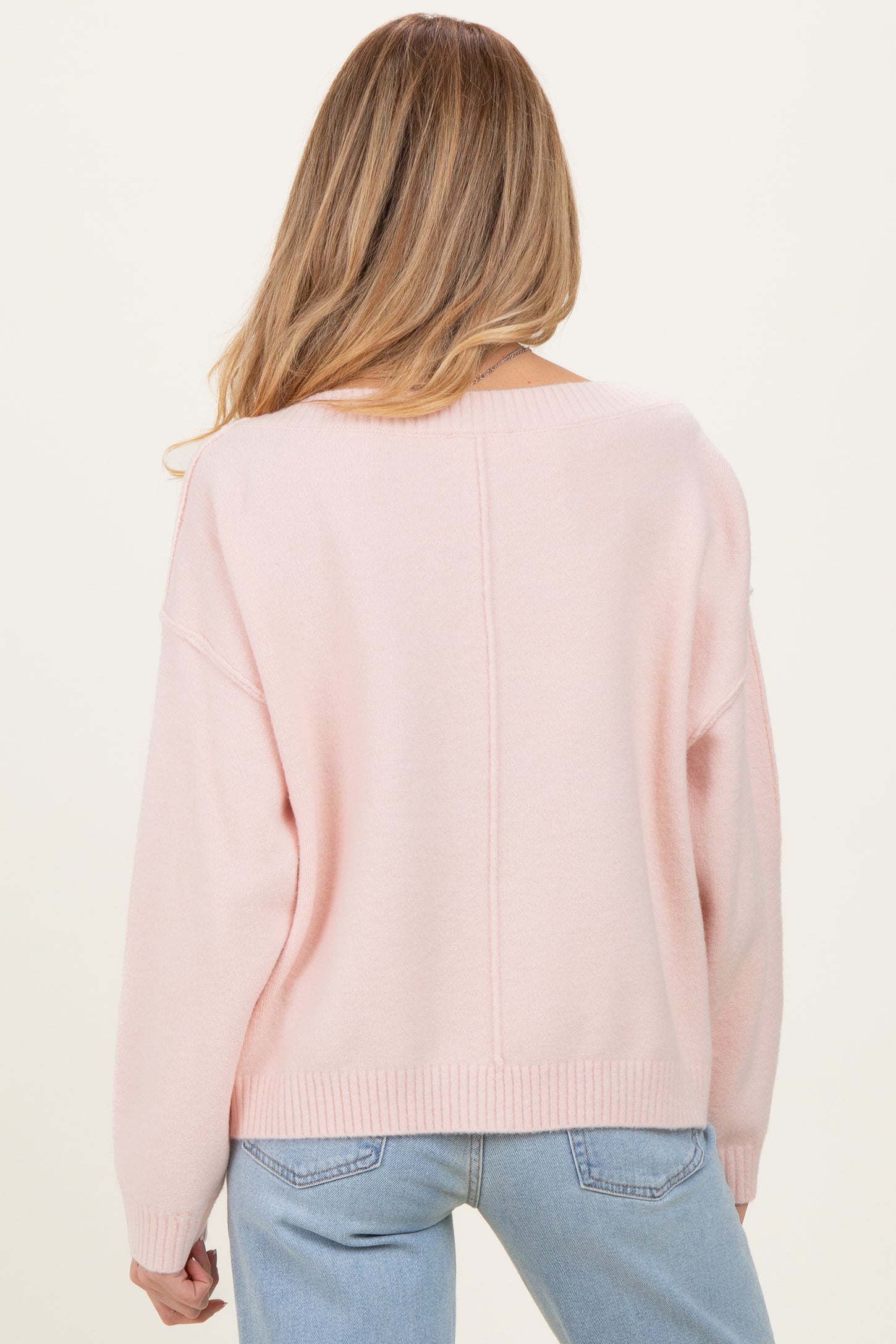 woman wearing a light pink maternity sweater with a loose fit and dropped shoulders, viewed from the back