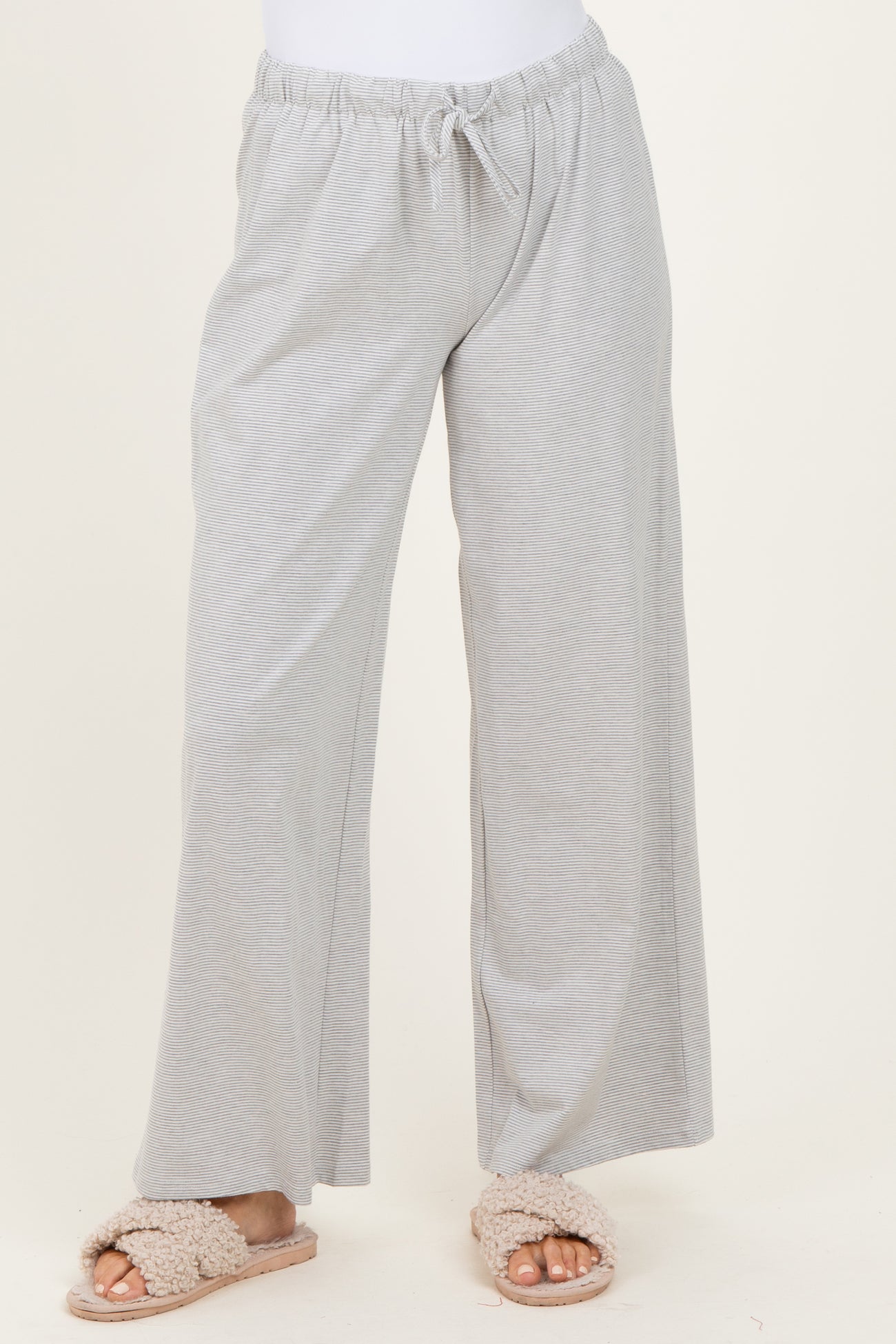 woman wearing light gray wide-leg lounge pants with an elastic waistband and drawstring detail, paired with fluffy slippers