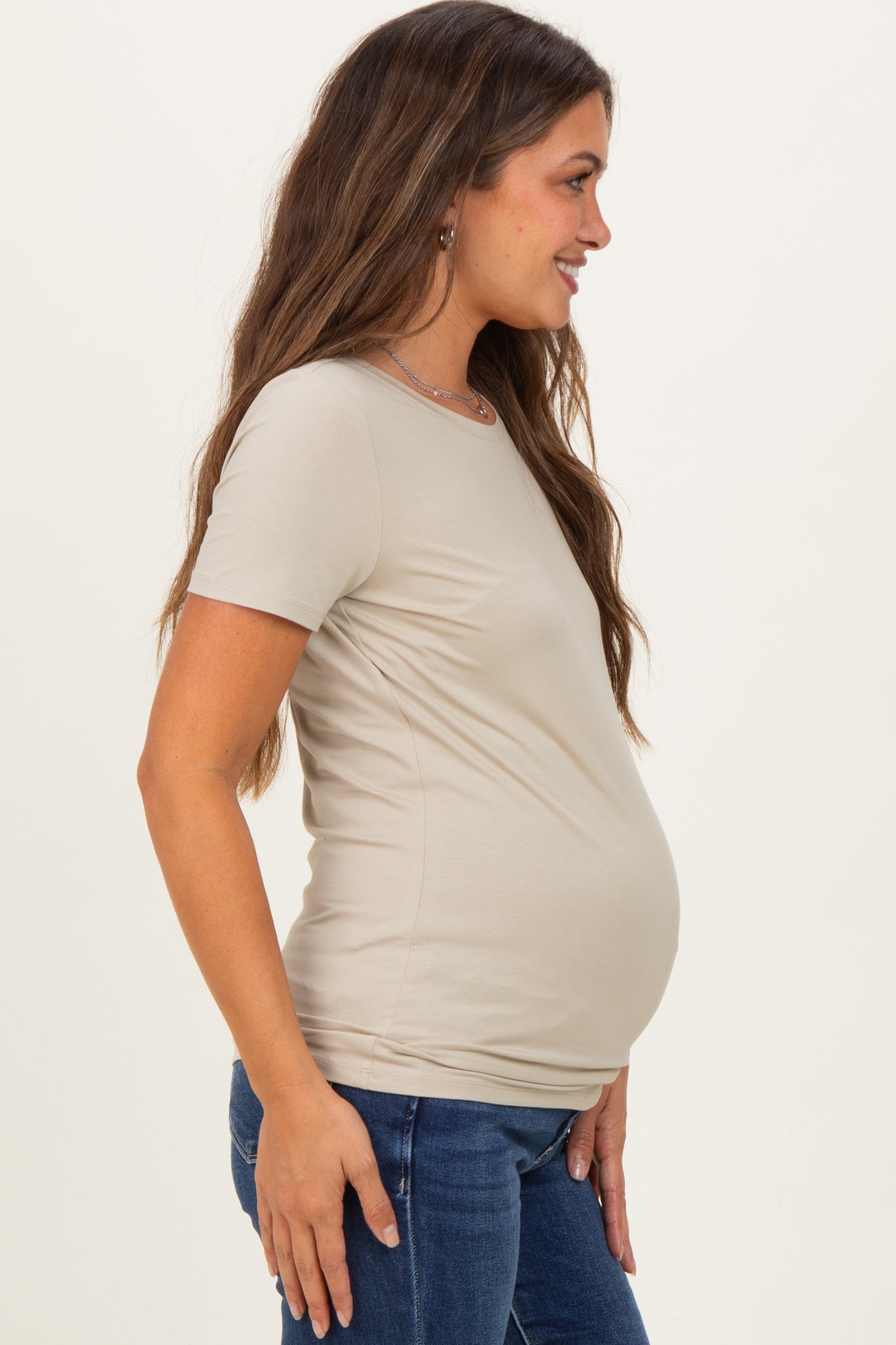 woman wearing a beige short sleeve maternity top and showing her baby bump