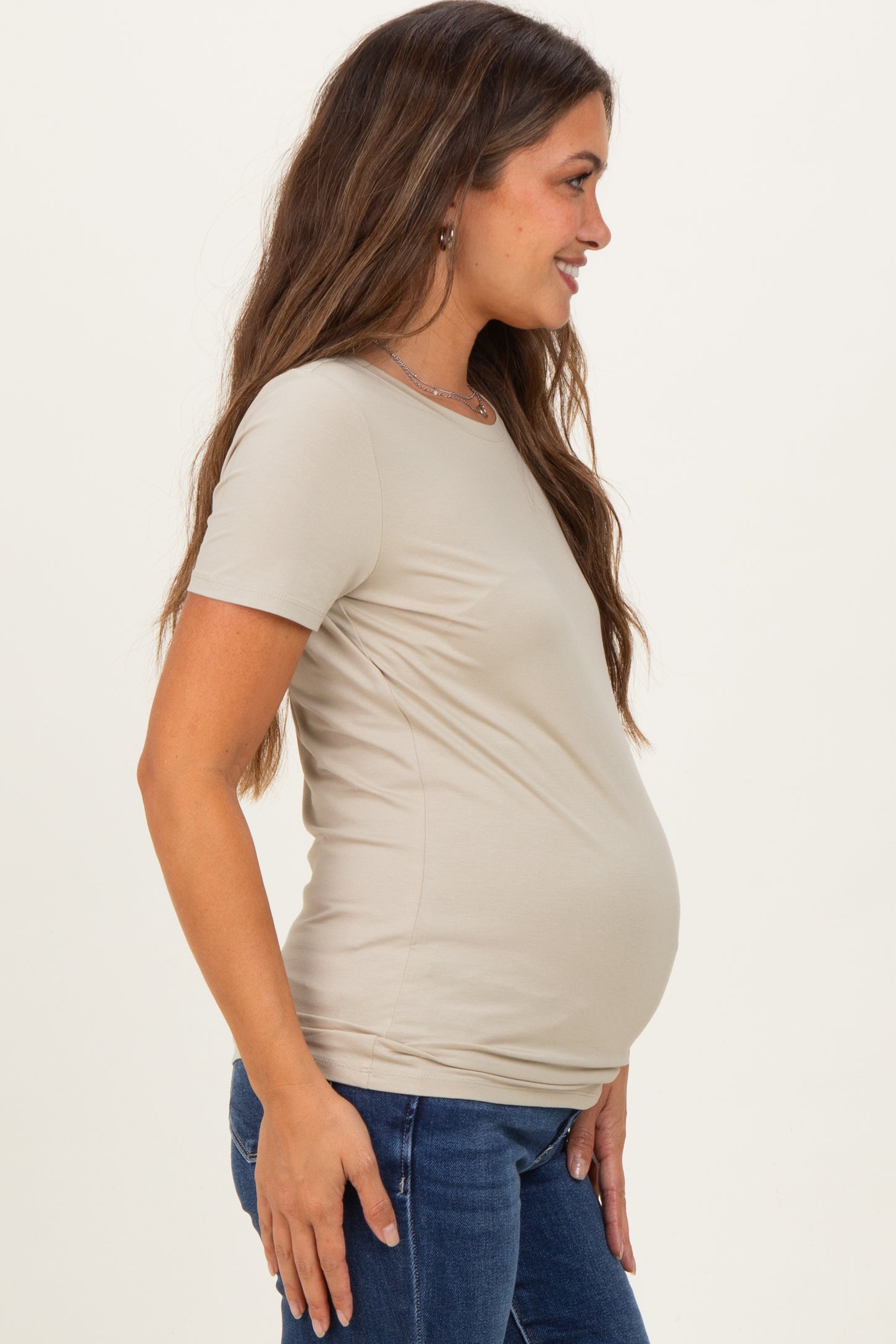 woman wearing a beige short sleeve maternity top and showing her baby bump