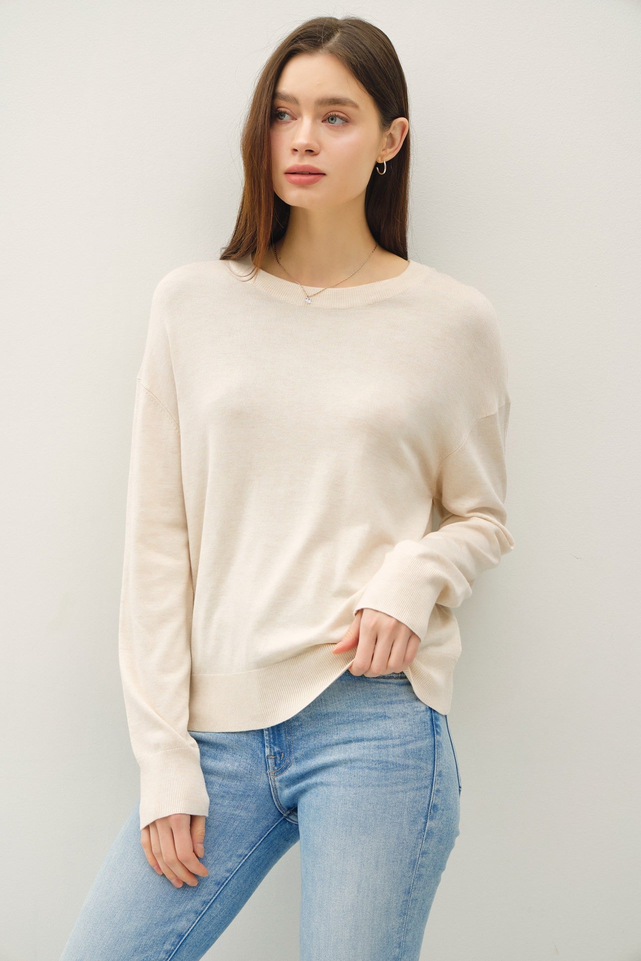 woman wearing a light beige long sleeve sweater paired with light blue jeans