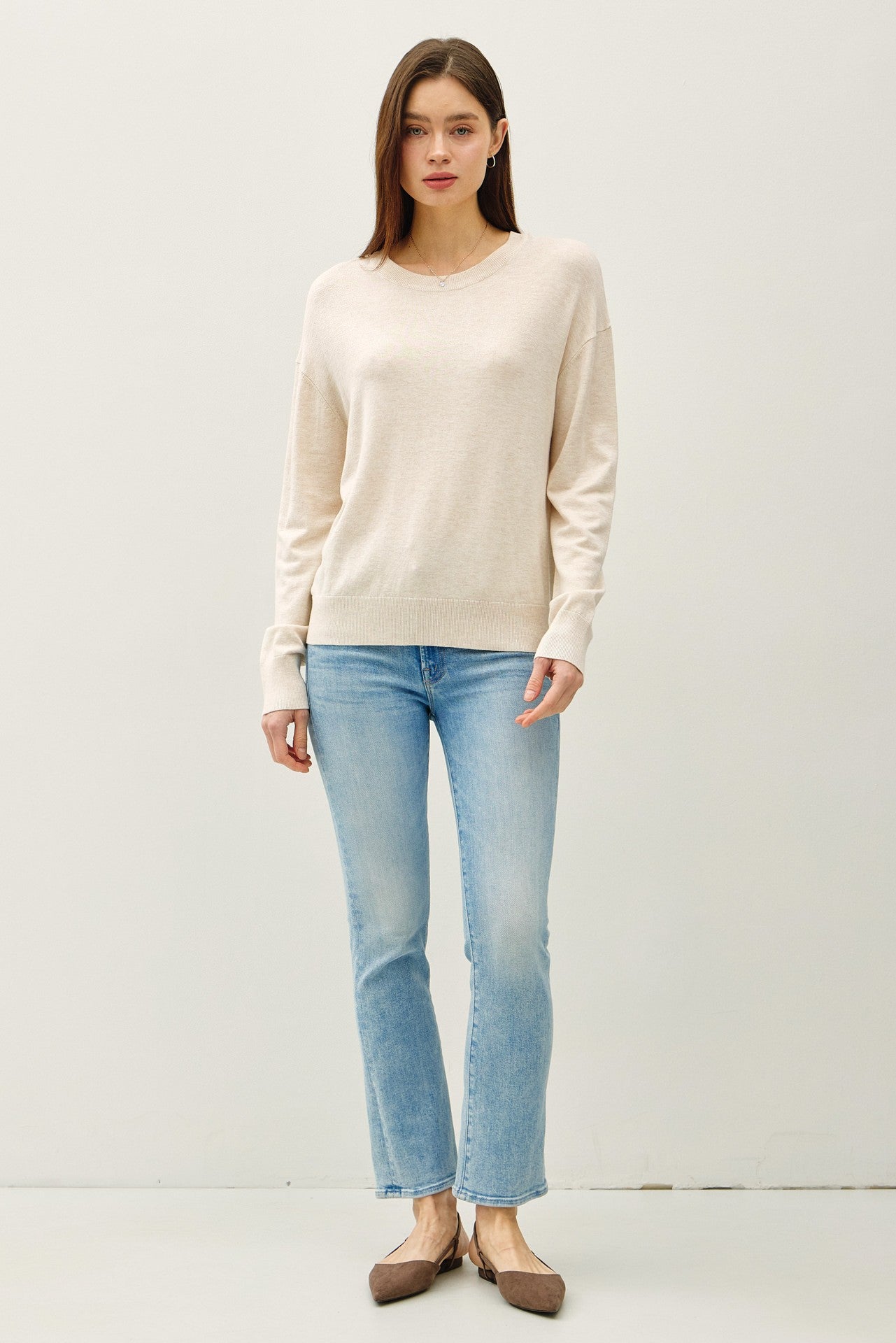 woman wearing a beige long sleeve sweater paired with light blue straight leg jeans and brown flats