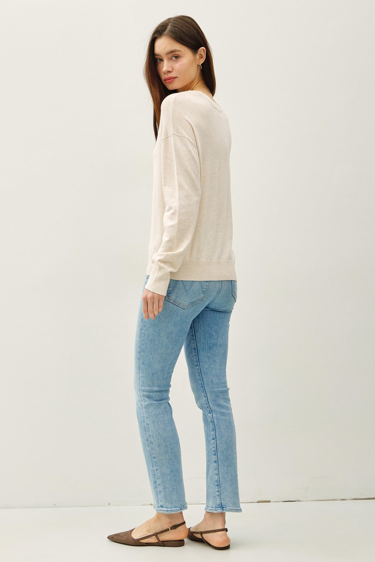 woman wearing a beige long sleeve sweater and light blue skinny jeans with brown flats