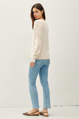 woman wearing a beige long sleeve sweater and light blue skinny jeans with brown flats