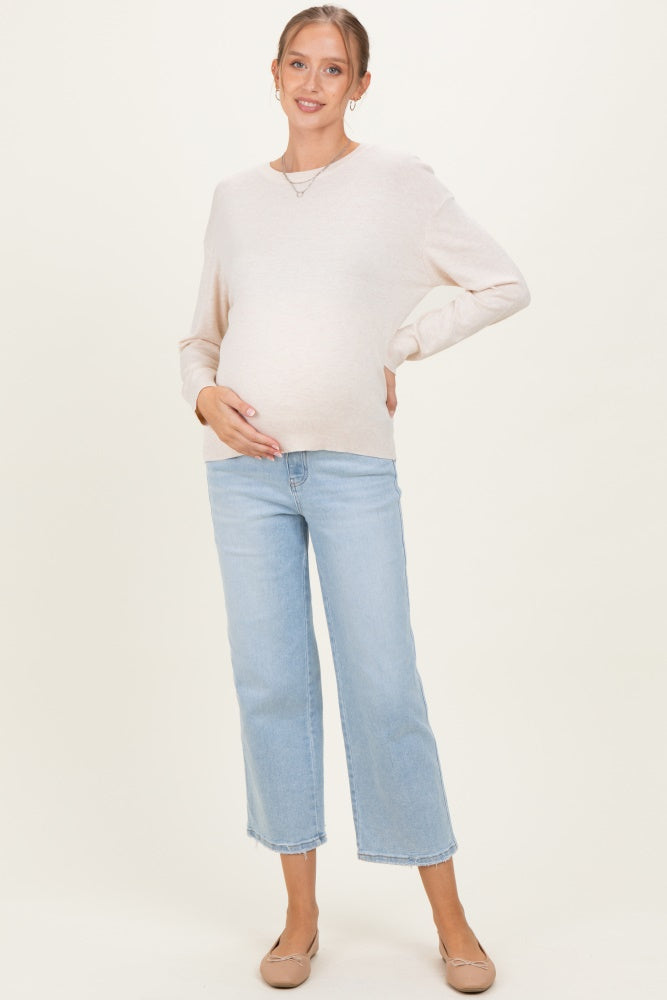 woman wearing a light beige long sleeve maternity sweater and blue cropped jeans, showing her baby bump