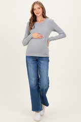 woman wearing a gray long sleeve maternity top and blue wide-leg jeans, gently holding her baby bump