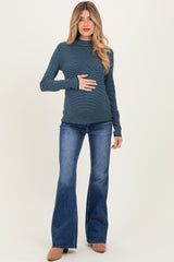 woman wearing a dark blue striped maternity long sleeve top and flared jeans, holding her baby bump