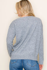 woman wearing a gray long sleeve sweater, shown from the back, with denim jeans