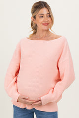 woman wearing a light pink oversized maternity sweater and holding her baby bump