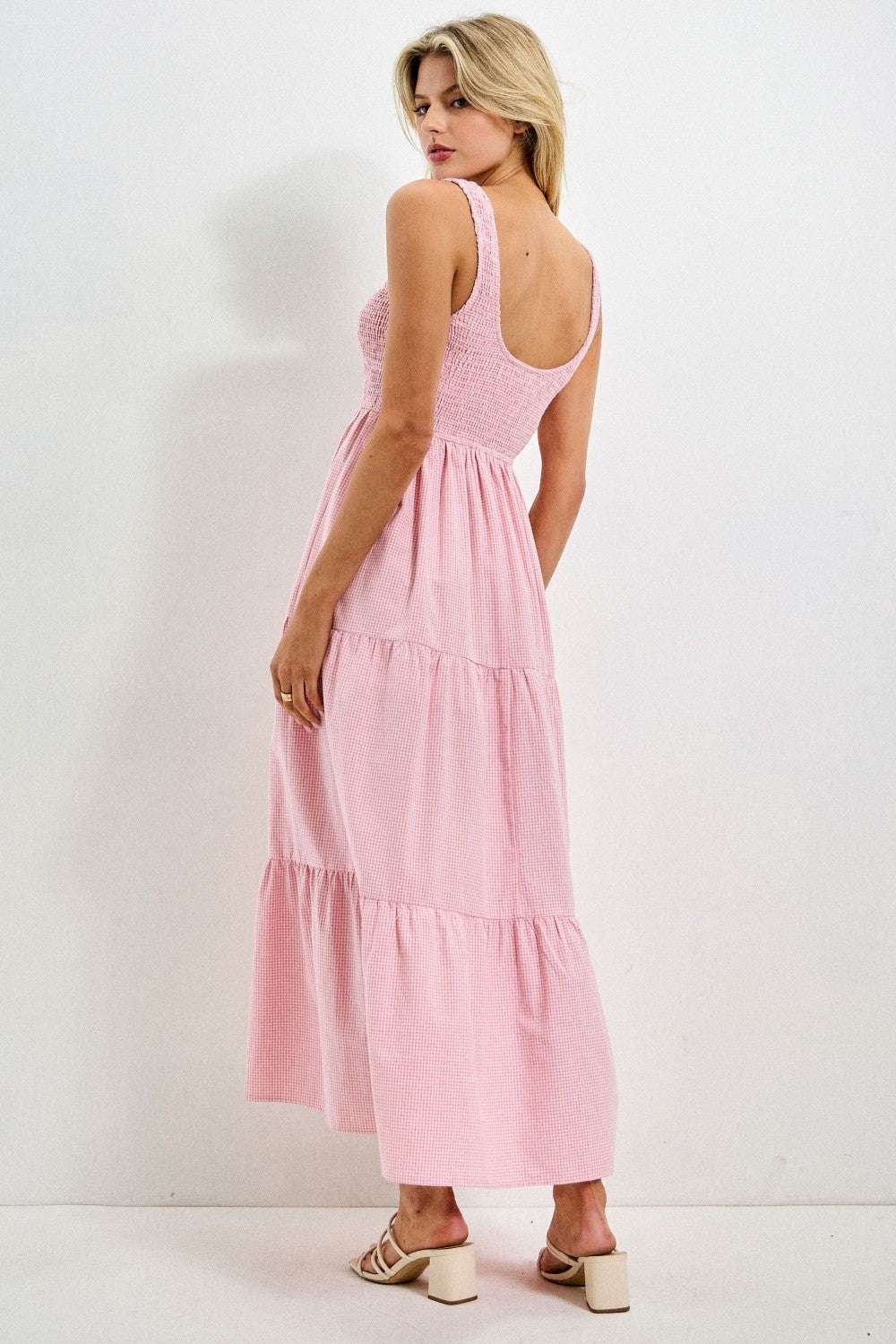 woman wearing a pink tiered maxi dress with smocked bodice and open back, styled with strappy heels