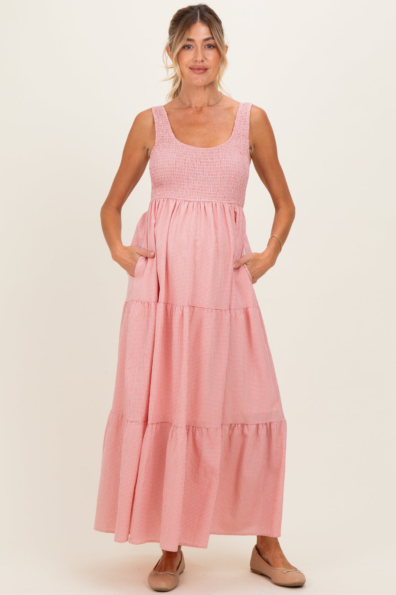 woman wearing a pink striped maternity maxi dress with a smocked bodice and pockets, showing her baby bump