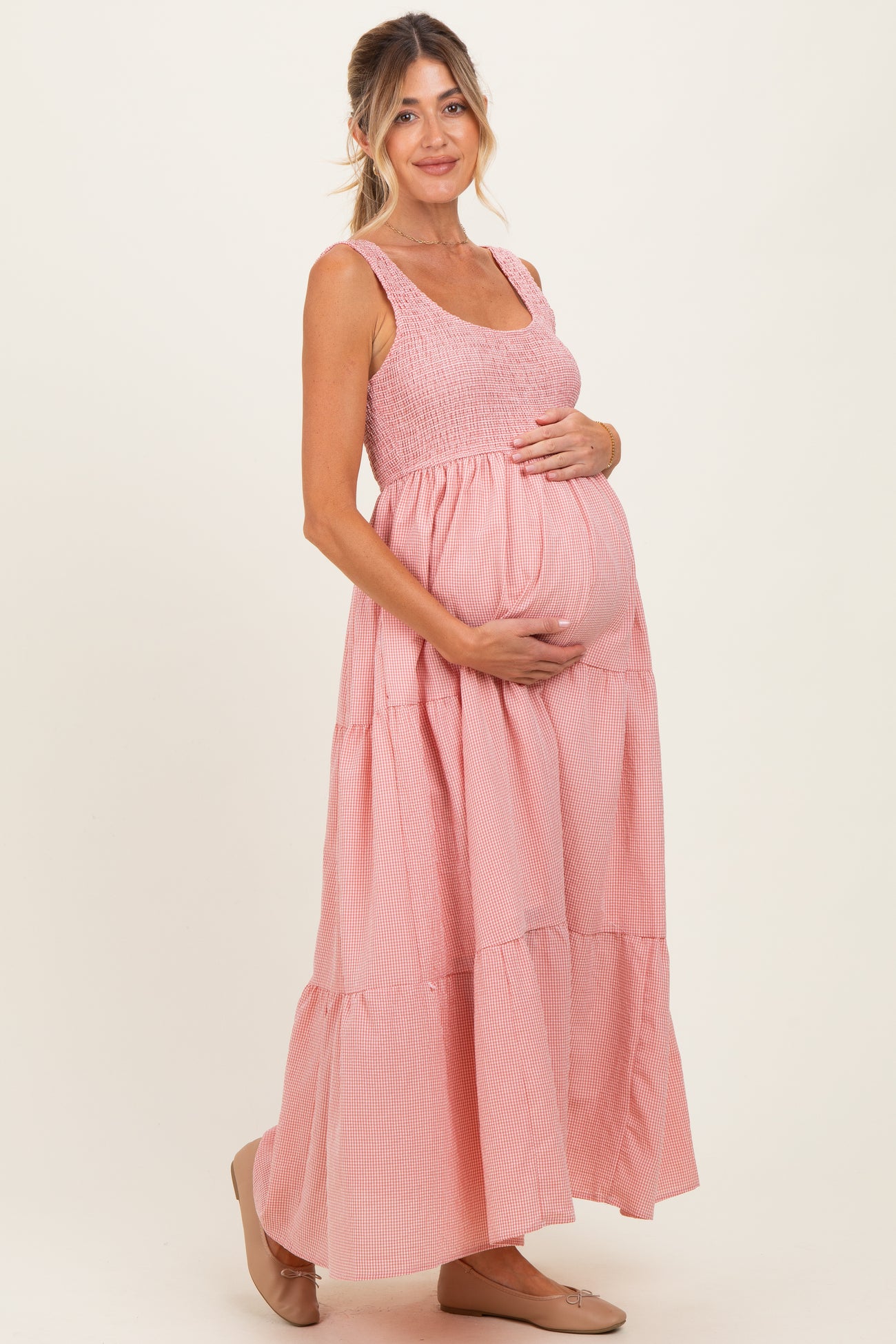 woman wearing a pink and white striped maternity dress with tiered design and holding her baby bump