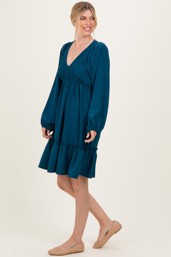 woman wearing a teal smocked v-neck dress with long puff sleeves and ruffled hem, standing in a side pose