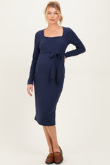 woman wearing a navy blue long sleeve maternity dress with a square neckline and tie waist, showcasing her baby bump