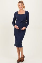 woman wearing a navy blue long sleeve maternity dress with a square neckline and a waist tie, showcasing her baby bump