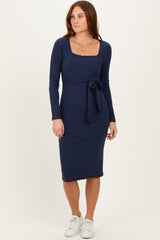 woman wearing a navy long sleeve fitted dress with a square neckline and waist tie detail