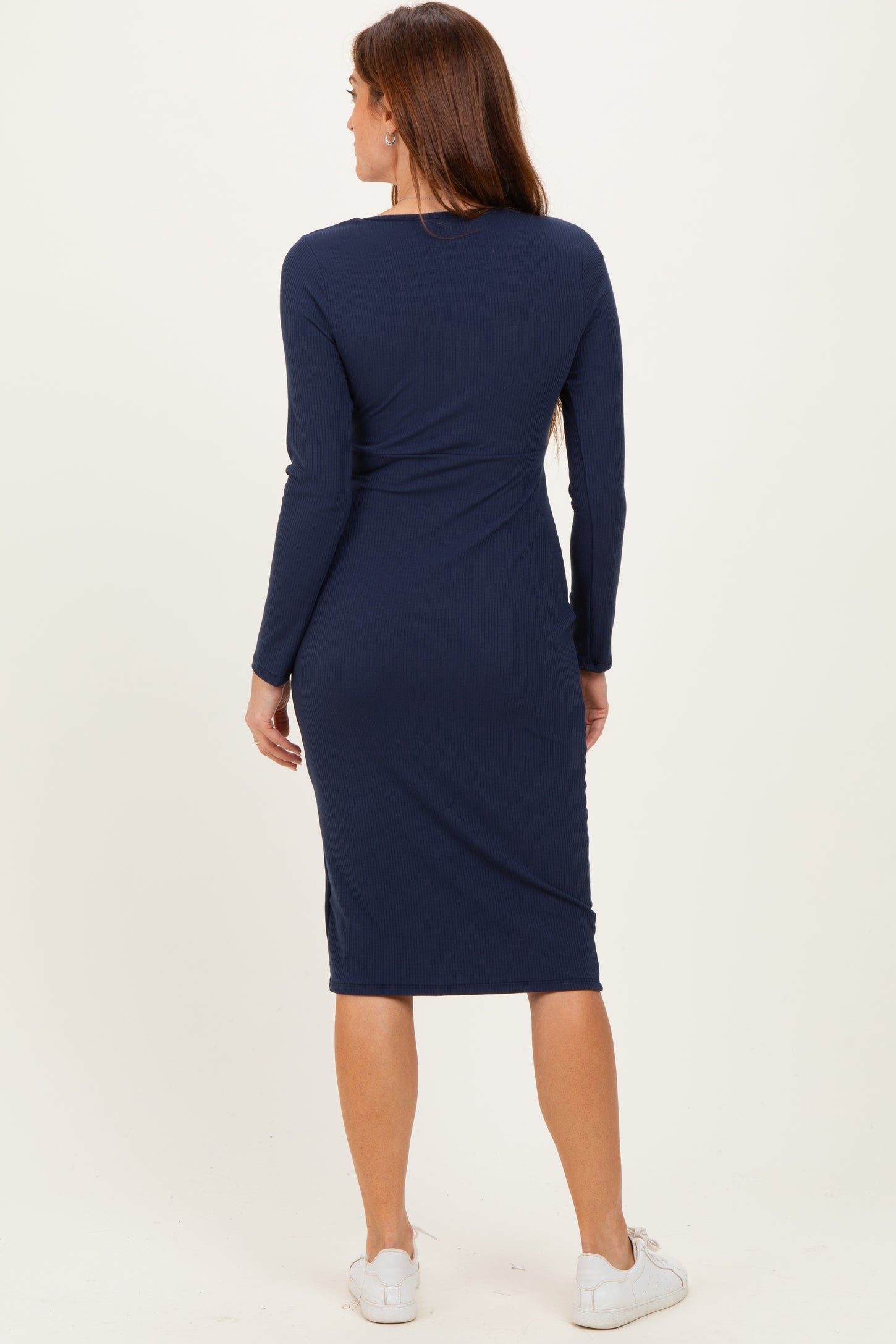 woman wearing a navy blue long sleeve midi dress with a fitted silhouette and white sneakers, shown from the back