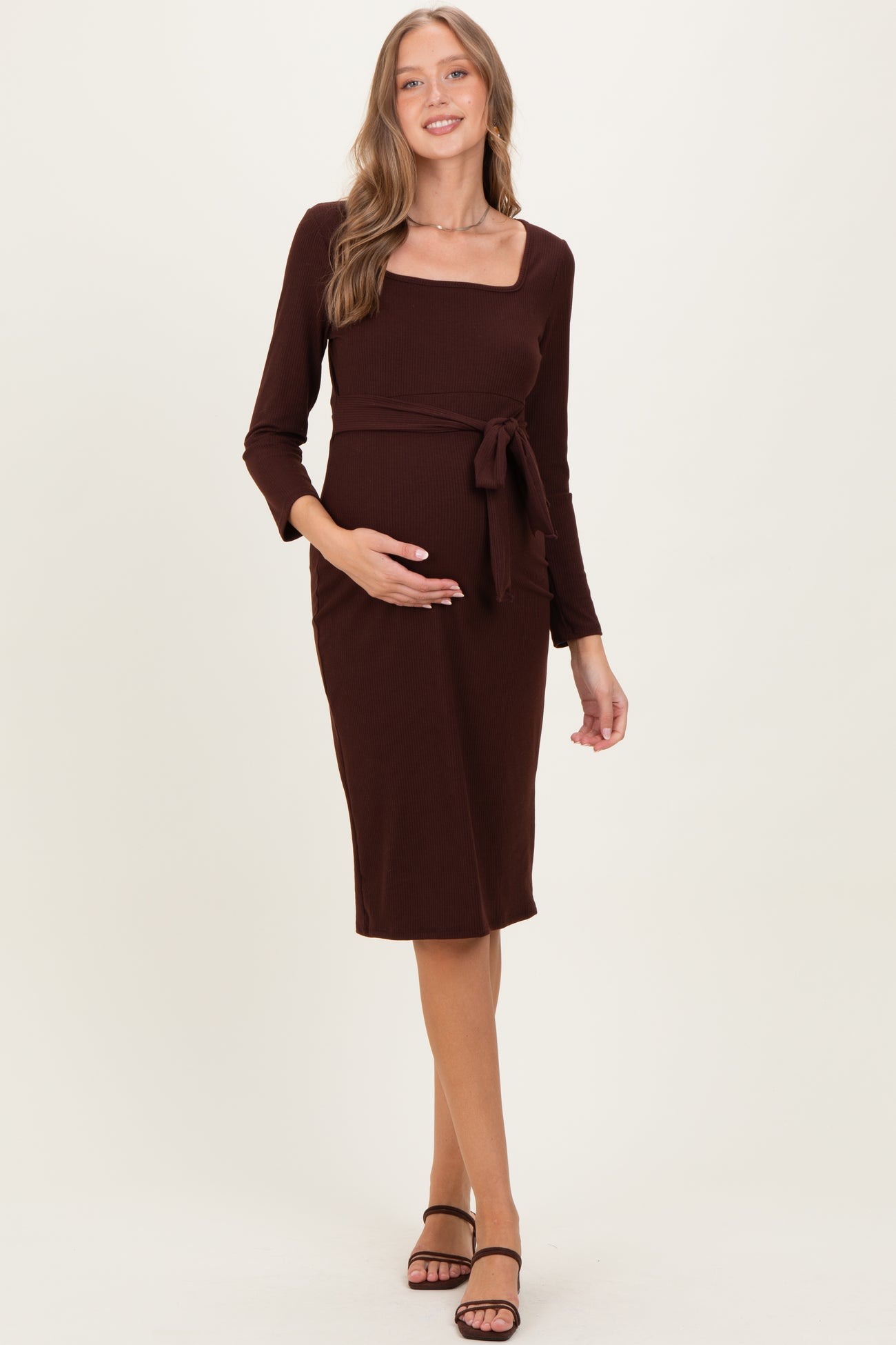 woman wearing a brown maternity midi dress with a square neckline and tie detail, highlighting her baby bump