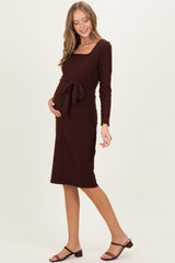 woman wearing a dark brown long sleeve maternity dress with a square neckline and tied waist, showing her baby bump