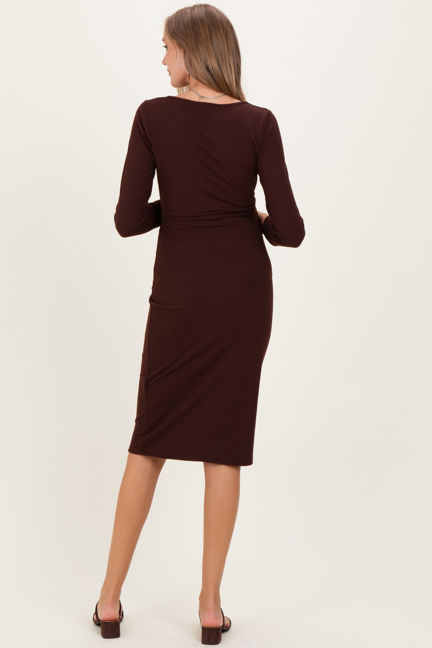 woman wearing a brown long sleeve maternity dress, seen from the back, fitted style with a midi length