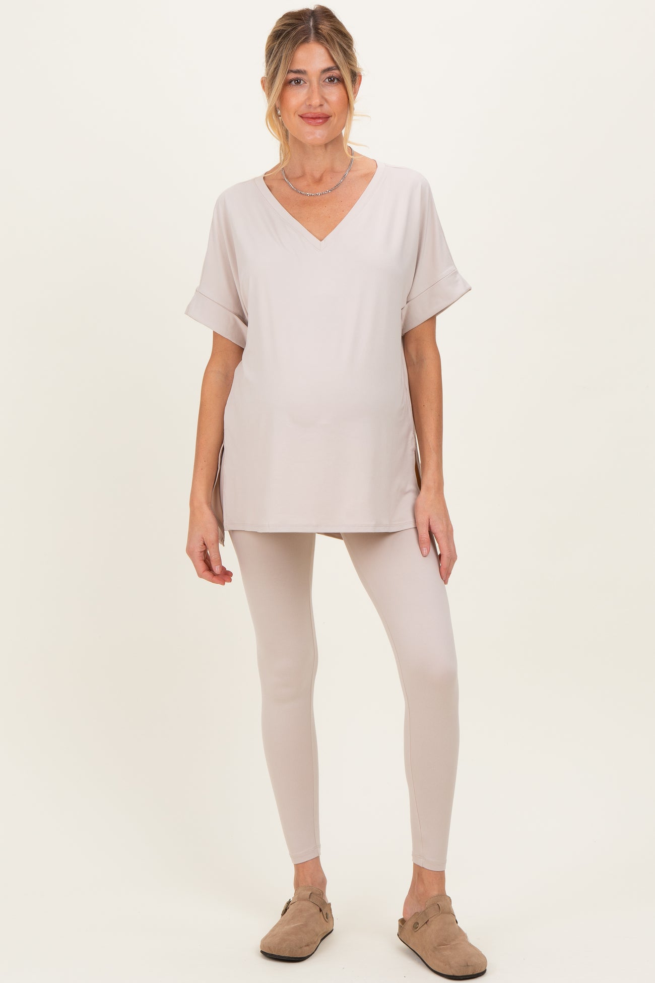 woman wearing a beige short sleeve maternity top and matching leggings, showing her baby bump