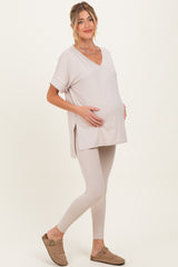 woman wearing a light beige maternity top and matching leggings, gently cradling her baby bump