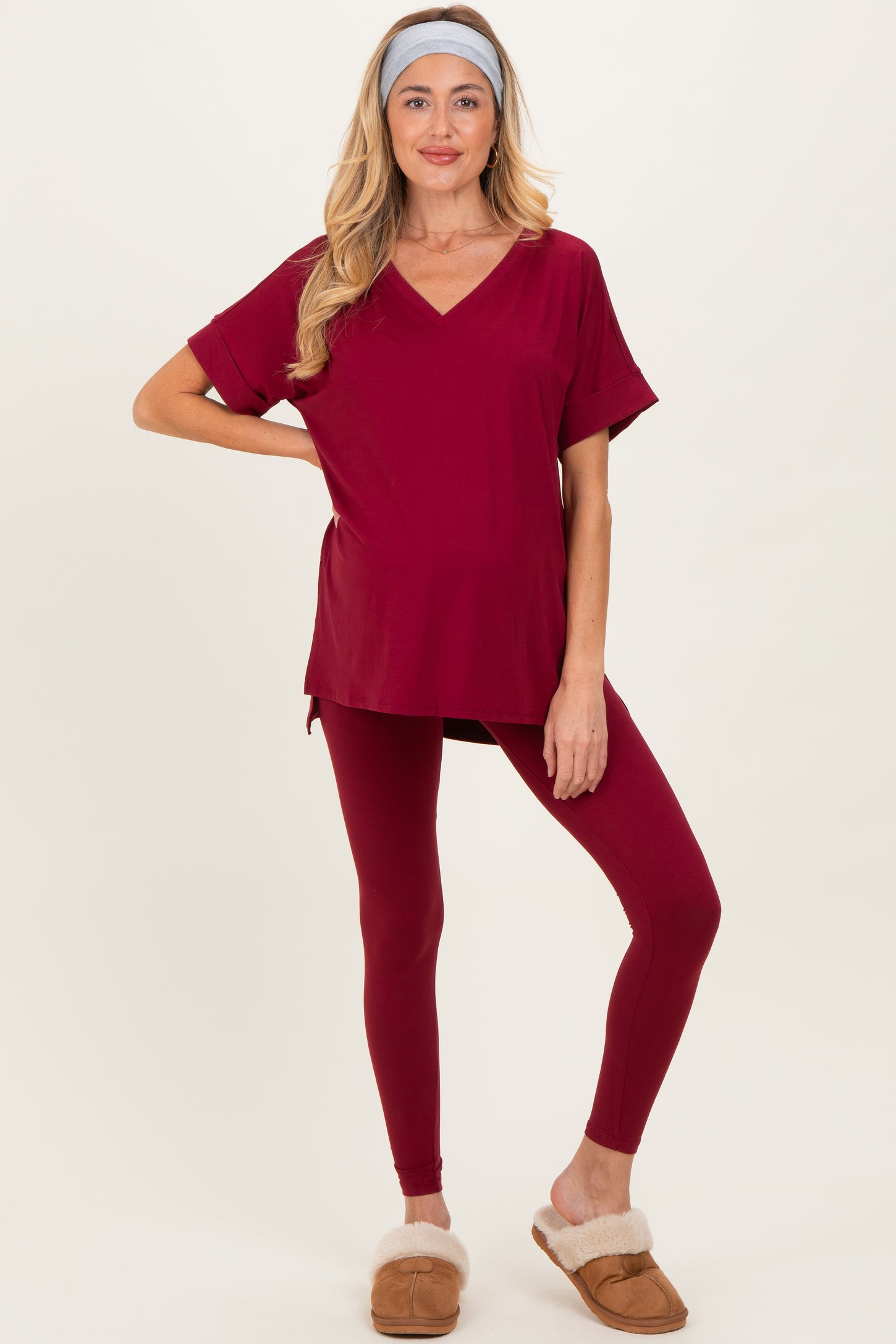 woman wearing a burgundy maternity top and matching leggings, showing her baby bump and styled with a headband and slippers
