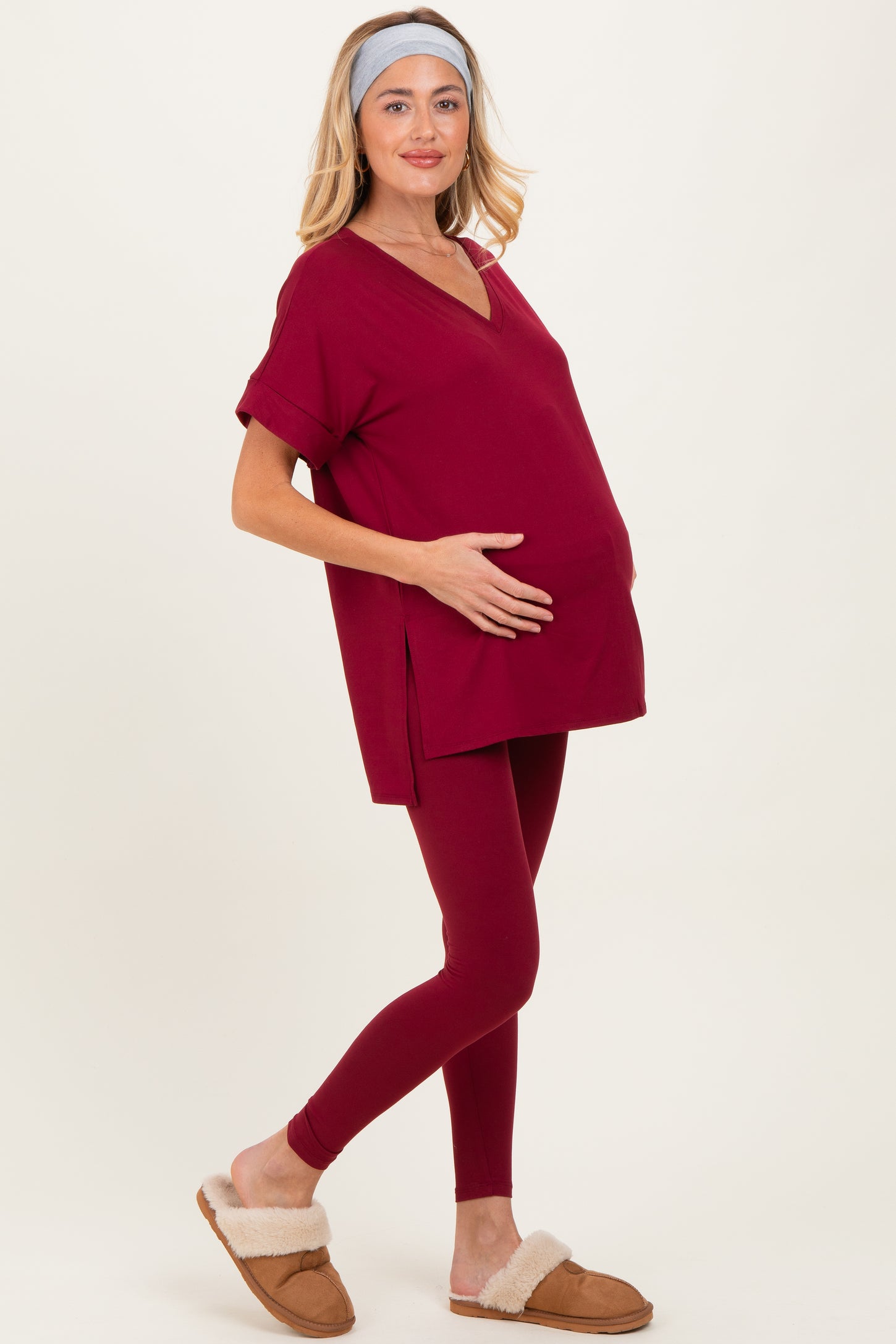 woman wearing a burgundy maternity top with a v-neck and matching leggings, holding her baby bump