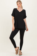 woman wearing a black v-neck oversized top with rolled sleeves and black leggings, standing in a relaxed pose