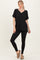 woman wearing a black v-neck oversized top with rolled sleeves and black leggings, standing in a relaxed pose