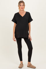 woman wearing a black v-neck maternity top and black leggings, showing a baby bump