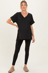 woman wearing a black maternity v-neck top with short sleeves and side slits, paired with black leggings and showing her baby bump