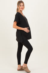 woman wearing a black short sleeve maternity top and black leggings, gently cradling her baby bump