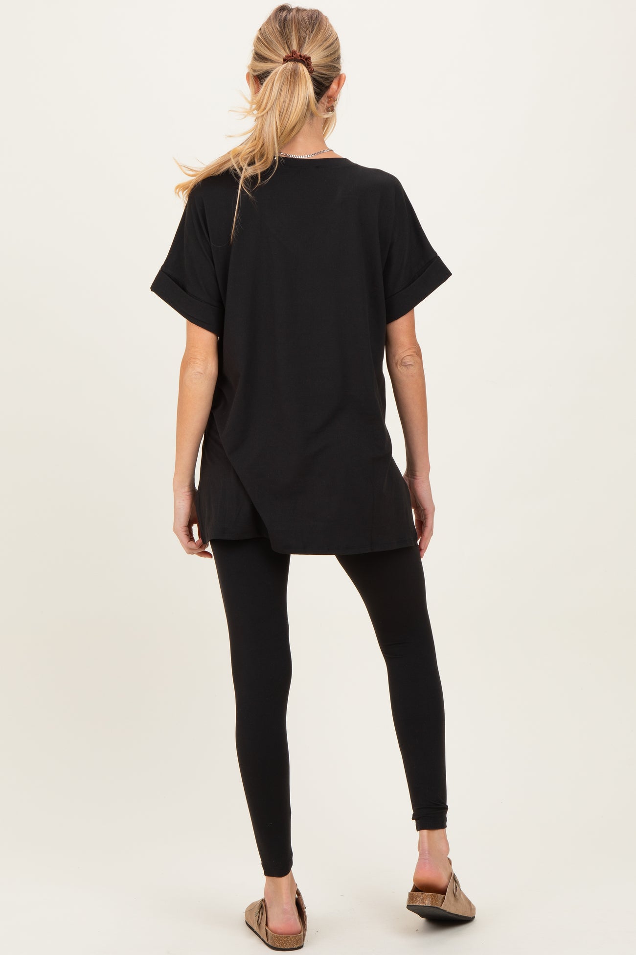 woman wearing a black oversized maternity top with rolled sleeves and black leggings, showing her back