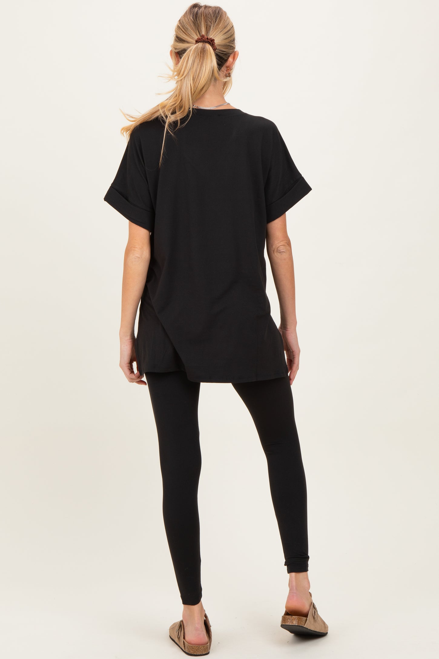 woman wearing a black oversized maternity top with rolled sleeves and black leggings, showing her back