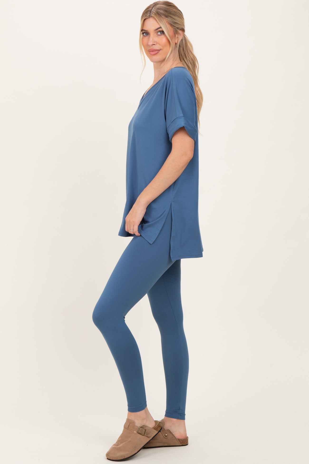 woman wearing a blue oversized top with short sleeves and matching leggings, standing sideways with hands in pockets