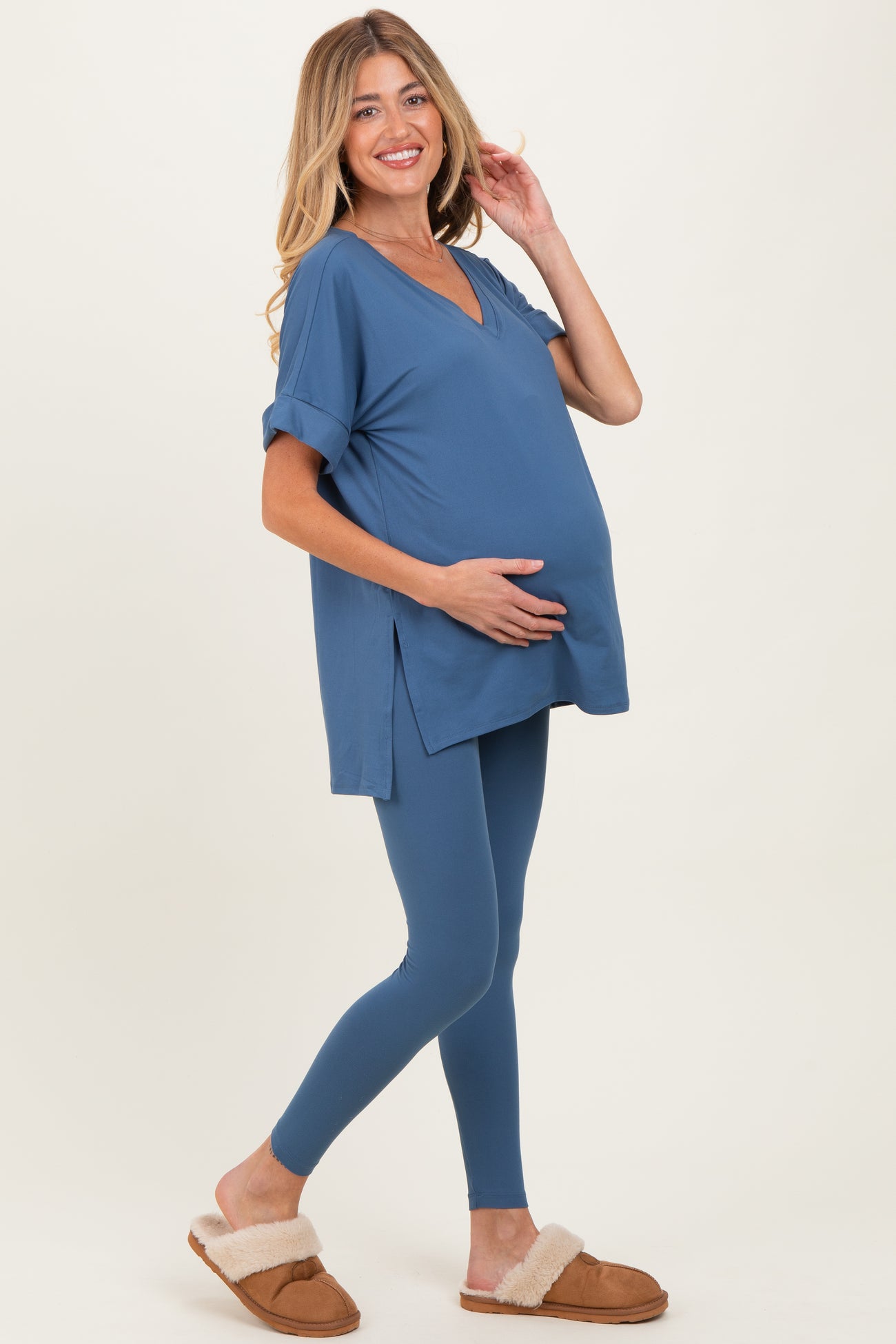 woman wearing a blue maternity top with a v-neck and rolled sleeves, holding her baby bump, paired with blue leggings